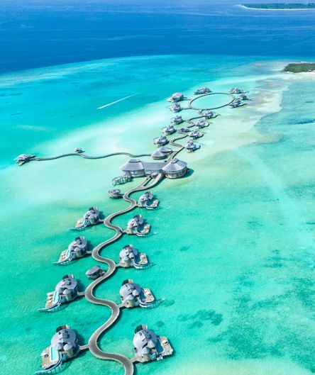 Exotisches Überwasser-Resort auf den Malediven mit geschwungenen Stegen und Villen im türkisfarbenen Ozean aus der Vogelperspektive.